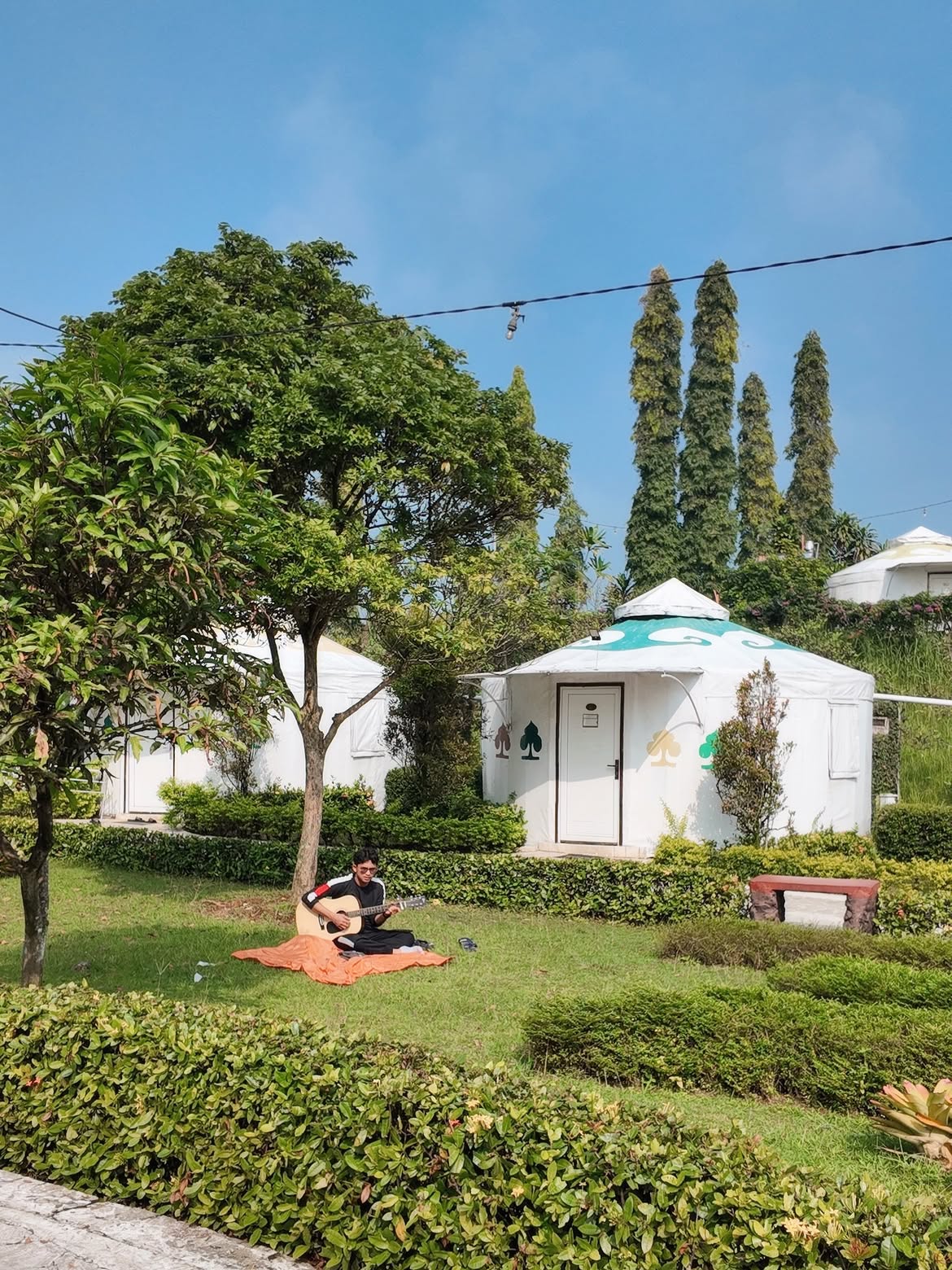 Keluarga sedang menikmati suasana alam di tempat glamping keluarga di Bogor dengan latar belakang pegunungan hijau yang asri